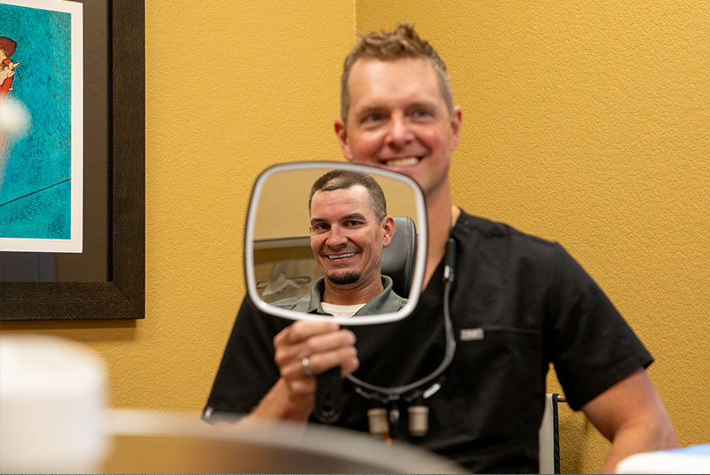 doctor holding up mirror for patient to see their smile after dental procedure